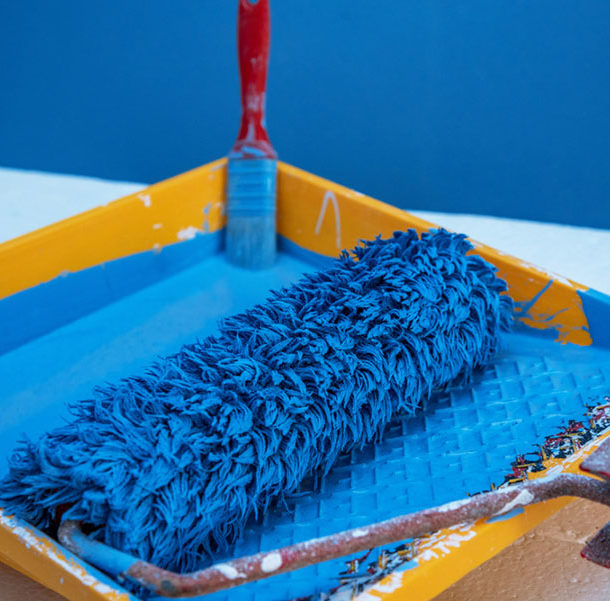 A blue paint roller in a yellow tray.