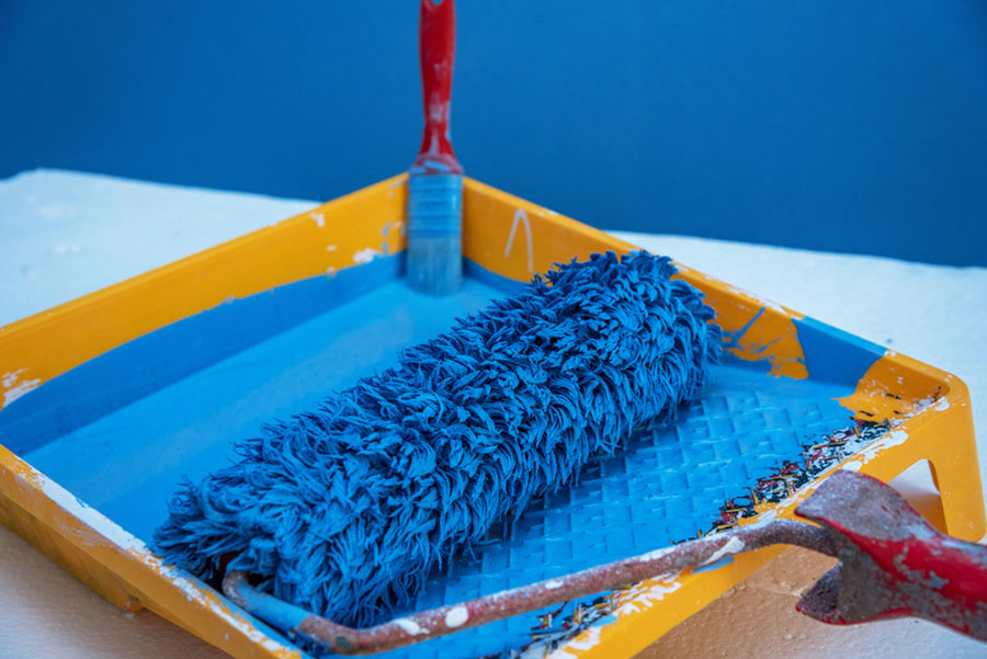 A blue paint roller in a yellow tray.