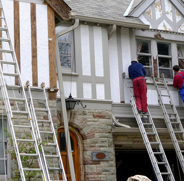 Two men on ladders in front of a house.